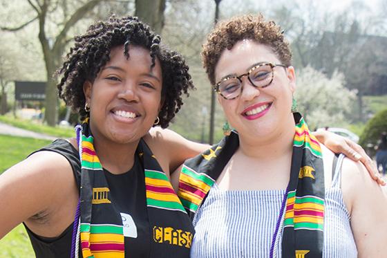 Photo of two Black women, graduating Chatham University students, wearing the multicultural graduation stole and smiling for the camera